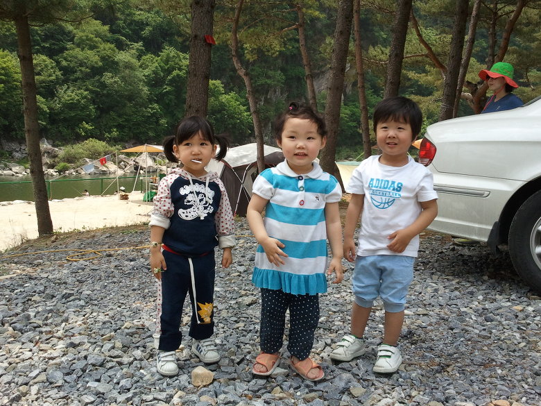 미소 짓는 세 아이, 캠핑장 강변 나무숲 배경